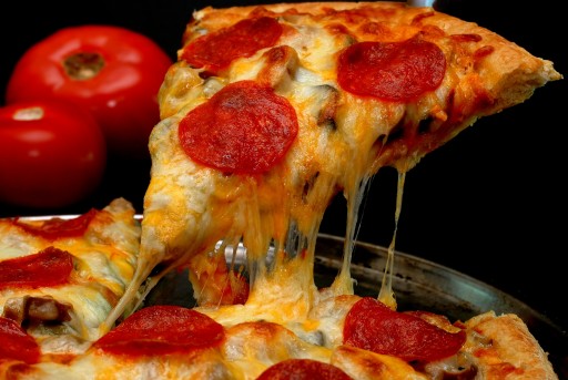Slice of pepperoni pizza being removed from whole pie with tomatoes in background. Isolated on black.